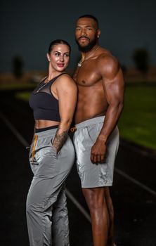 A fit couple posing in fashionable sportswear on an outdoor track.
