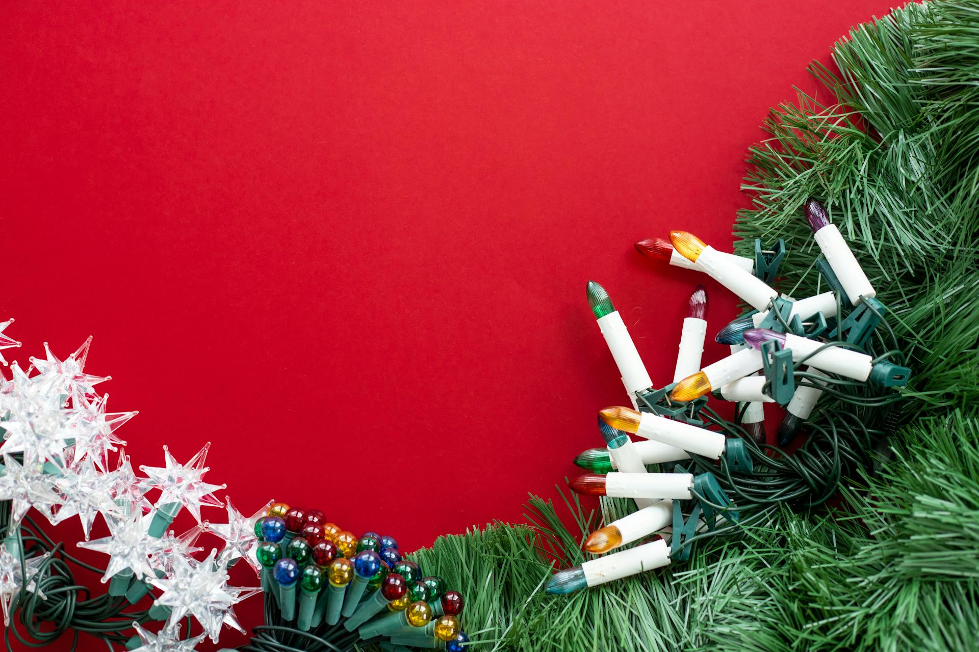 Christmas decorations featuring garland and colorful lights on a vibrant red background.