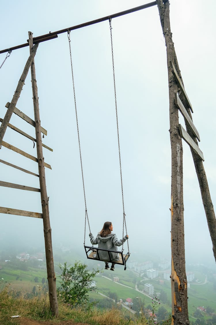 Woman Sitting On A Tall Wooden Swing Overlooking A Fog-Shrouded Valley