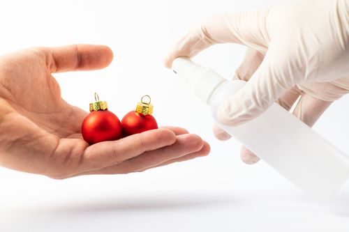 Free Close-up of hands spraying disinfectant on red Christmas baubles for holiday hygiene. Stock Photo