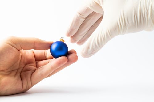 Free A blue Christmas ornament being handed over by a gloved hand on a white background. Stock Photo