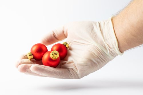 Free A latex-gloved hand holding three red Christmas baubles on a white background. Stock Photo