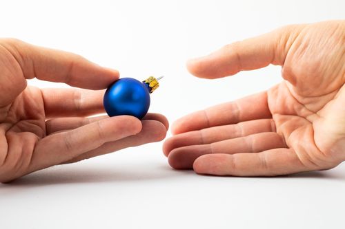 Free Hands exchanging a blue Christmas ornament, perfect for holiday themes. Stock Photo