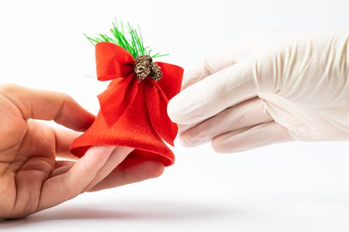 Free Close-up of a festive red bell Christmas ornament being held by hands wearing white gloves. Stock Photo