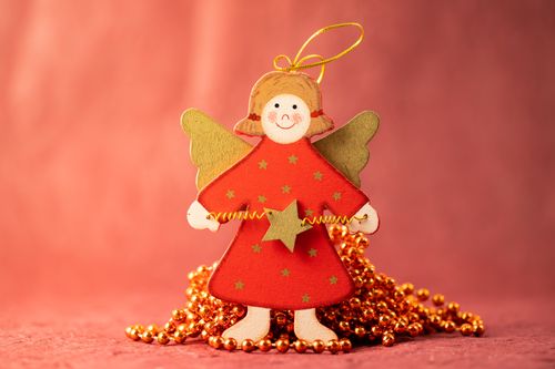Free A charming handmade wooden angel ornament on a red background, perfect for holiday decorations. Stock Photo