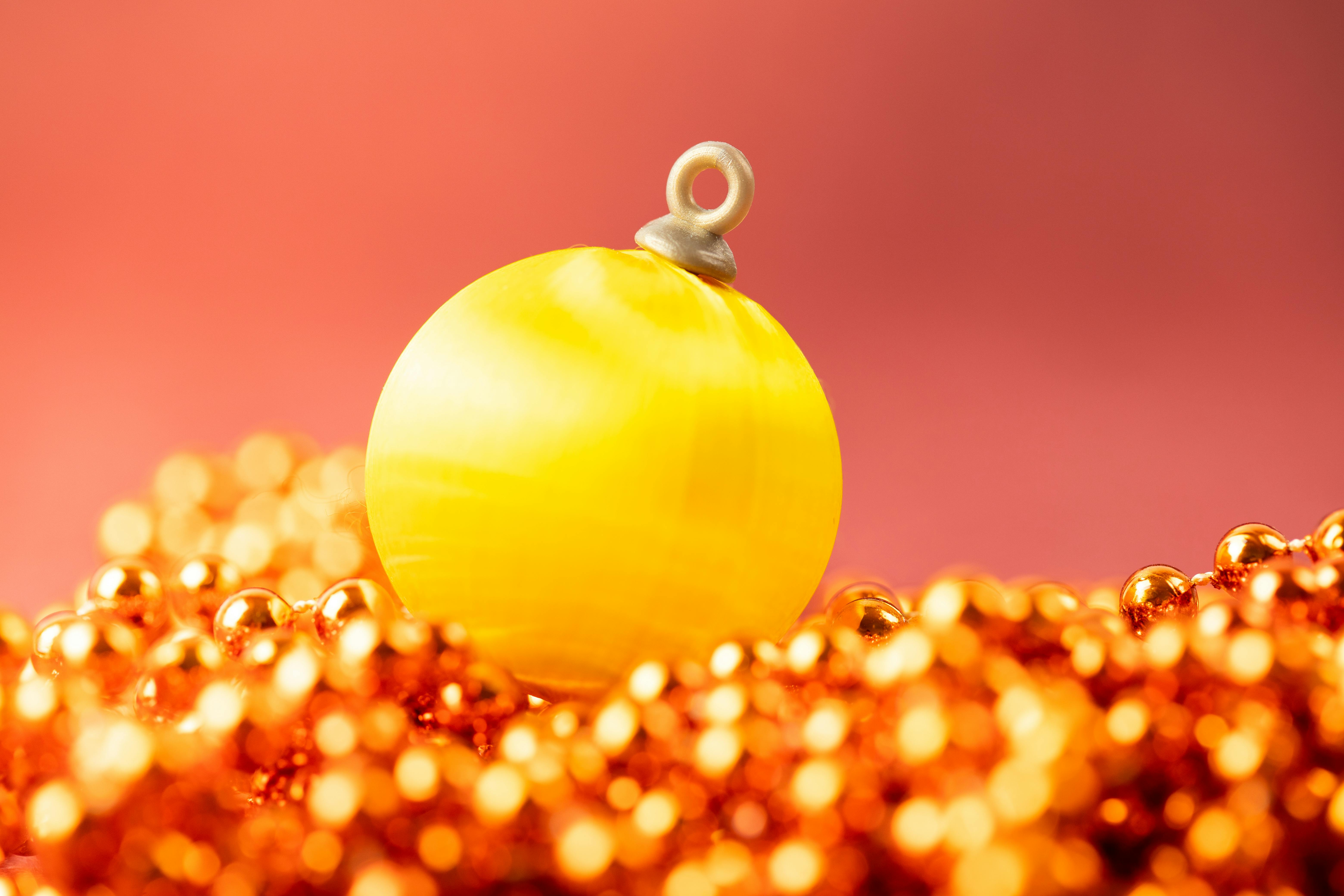 Bright yellow Christmas bauble with festive beads in a warm, vibrant setting.