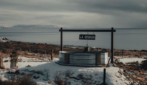 Free A serene winter landscape featuring a rustic well by a calm seacoast under overcast skies. Stock Photo