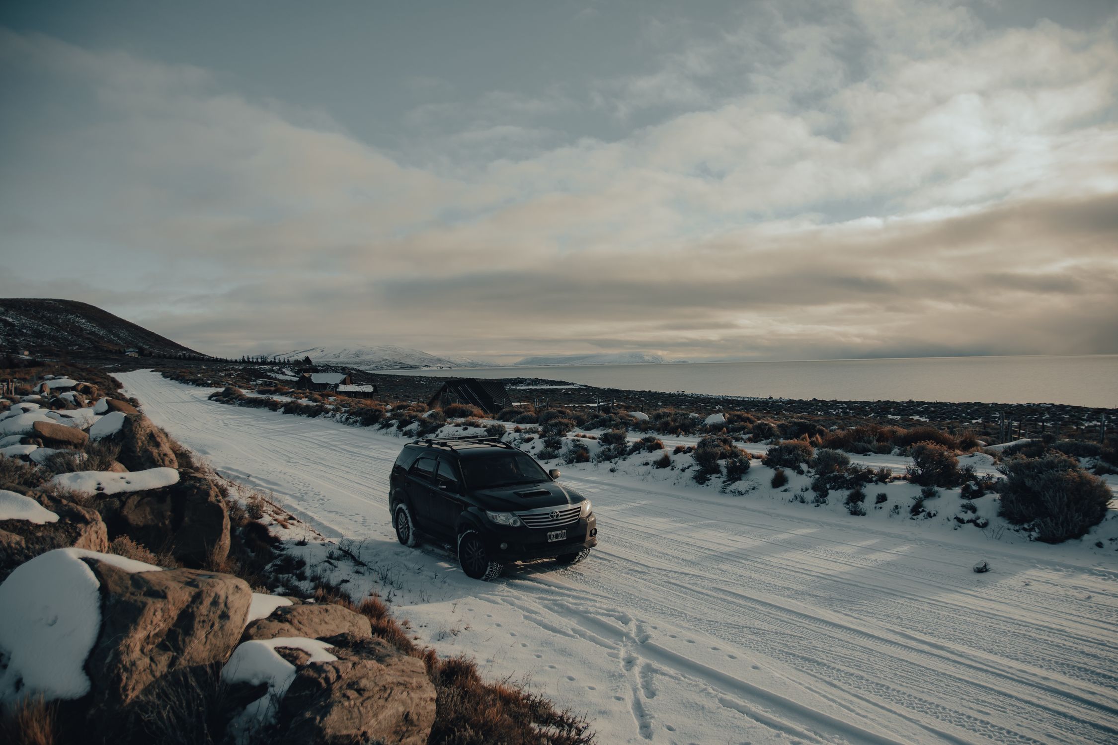 Black SUV driving on a snow-covered road through a scenic winter landscape.