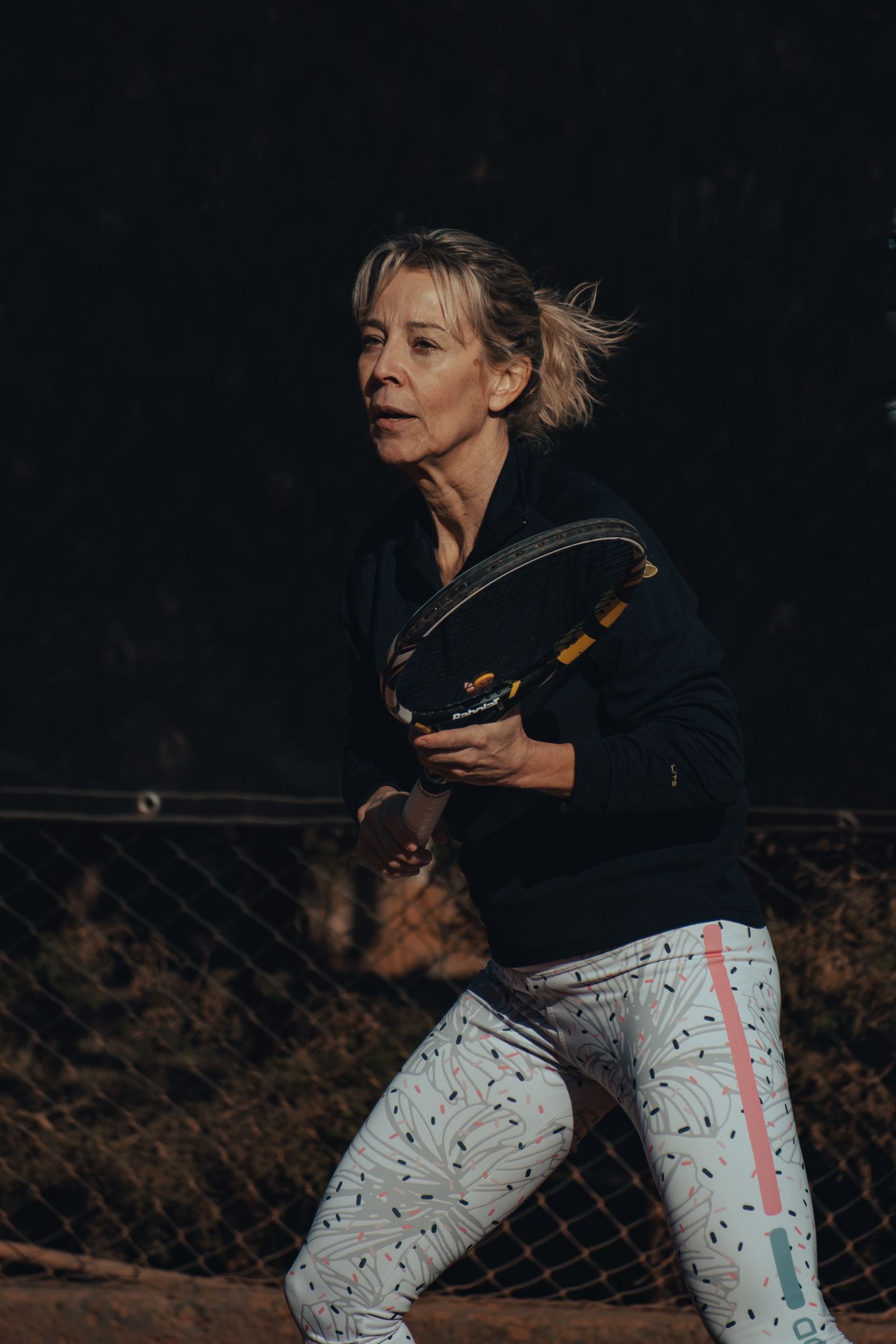Mature woman preparing to return a tennis ball on an outdoor court