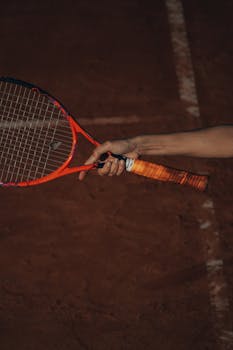 A tennis player holding a racket on a clay court, emphasizing grip and sport dynamics.