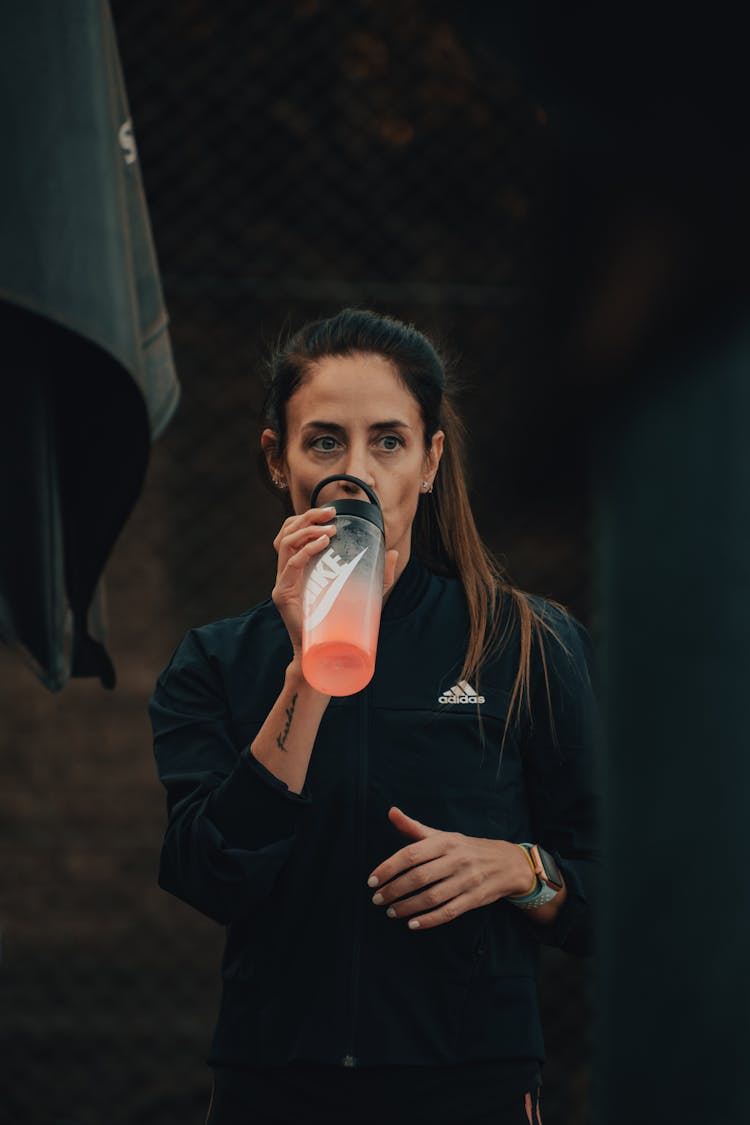 A Woman In A Black Jacket Drinking Using Water Bottle