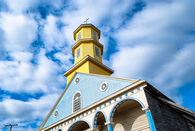 Yellow Tower Of The Church Of Chonchi In Chile Under Blue Sky And White Clouds