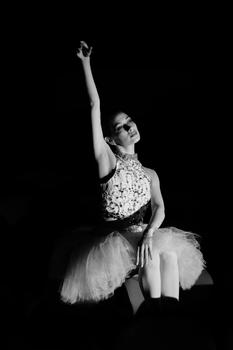 Black and white portrait of a ballet dancer sitting gracefully with hand raised, showcasing elegance and poise.