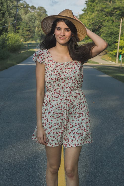Woman Wearing a Straw Hat and a Floral Romper Standing in the Middle of a Road