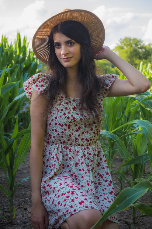 Free Elegant woman wearing a floral dress and straw hat, posing in a lush green cornfield during daytime. Stock Photo