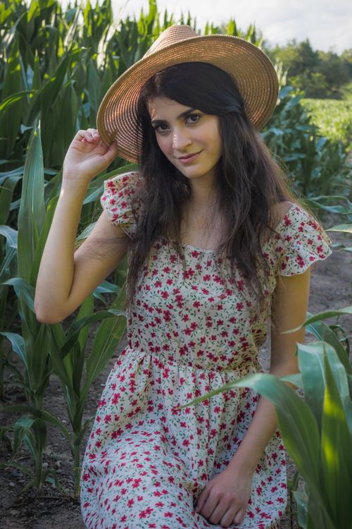 Free A young woman poses stylishly in a floral dress and sunhat amidst lush greenery. Stock Photo