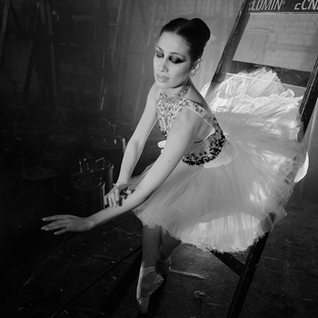 Elegant ballerina in a tutu gracefully poses on a ladder in a dramatic, moody setting.（イメージ）