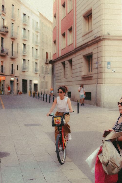 Free A woman enjoys a leisurely ride on a bicycle through a charming European street on a sunny day. Stock Photo