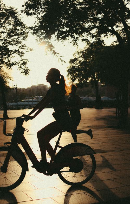 Free A woman cycling outdoors with a vibrant sunset backdrop, creating a beautiful silhouette. Stock Photo