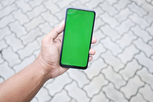 Close-up of a hand holding a smartphone with a green screen, ideal for mockups.