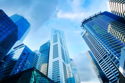 A breathtaking low angle view of modern skyscrapers with glass and concrete facades under a blue sky.