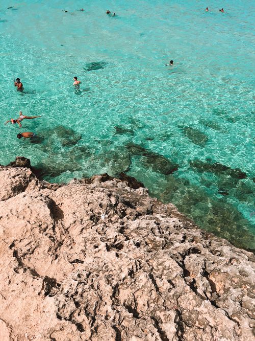 Free Aerial view of swimmers enjoying clear turquoise ocean waters next to rocky shore. Stock Photo