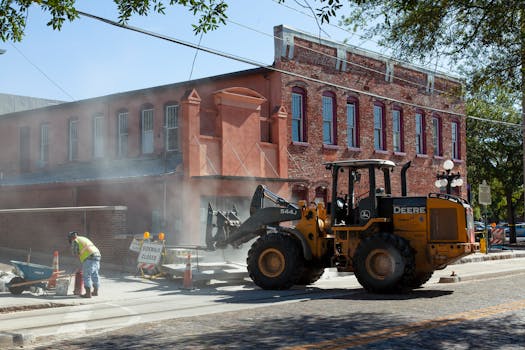 Street construction with machinery and workers by a brick building.