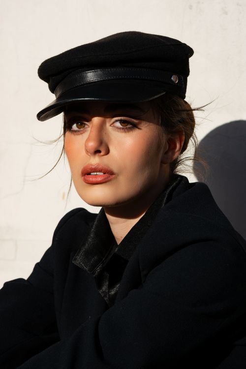 Free Stylish portrait of a woman in a black cap and coat against a white backdrop. Stock Photo