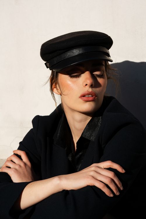 Free Fashionable portrait of a woman wearing a black cap and coat against a light background. Stock Photo