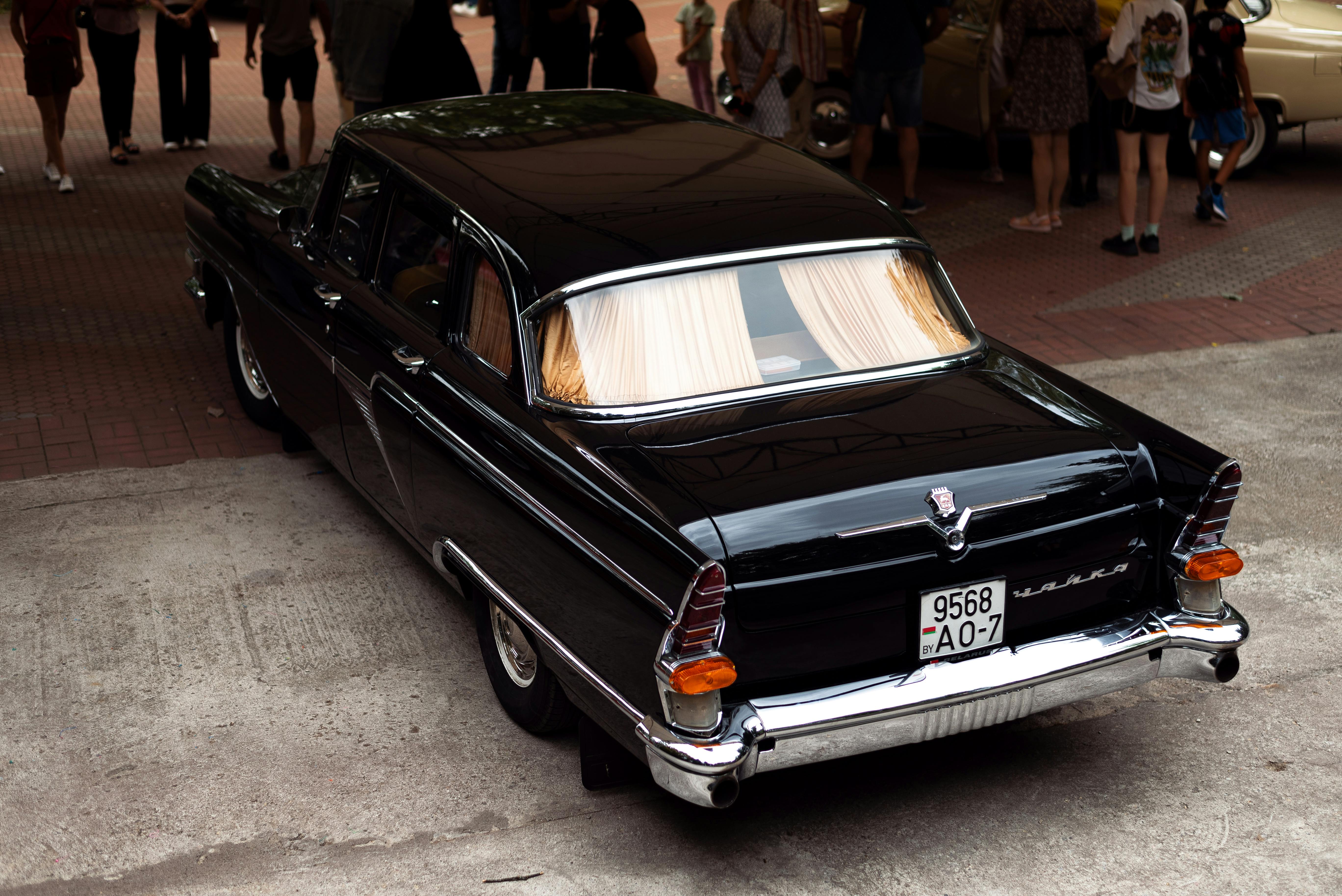 Classic black car displayed at an outdoor vintage auto show, surrounded by people.