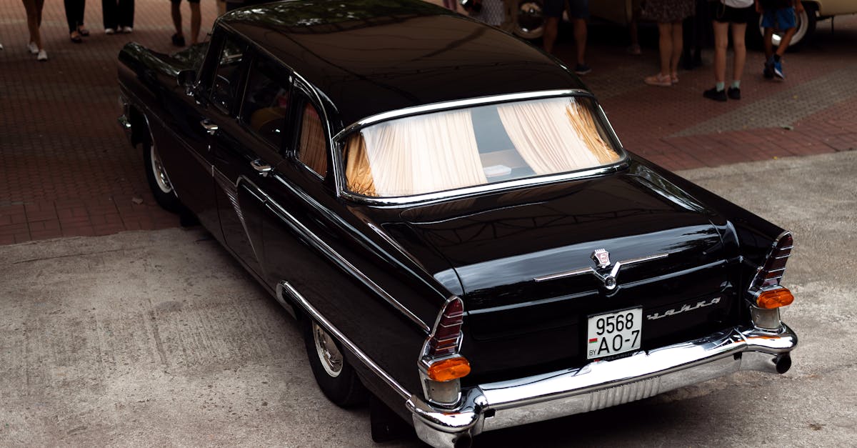 Classic black car displayed at an outdoor vintage auto show, surrounded by people.