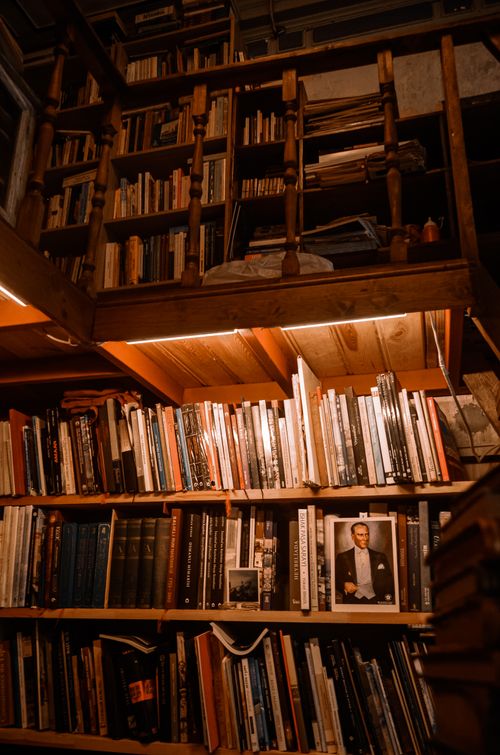 Free A wooden bookshelf in a cozy library setting with warm ambient lighting and various books. Stock Photo