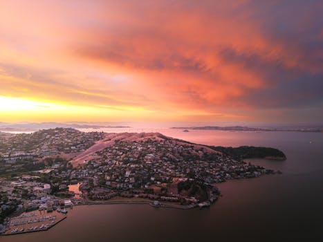 A breathtaking aerial view of a coastal town at sunset with vibrant sky and ocean.