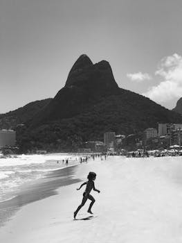 A child runs joyfully on the black and white sands of Ipanema Beach with Rio's iconic mountain backdrop.