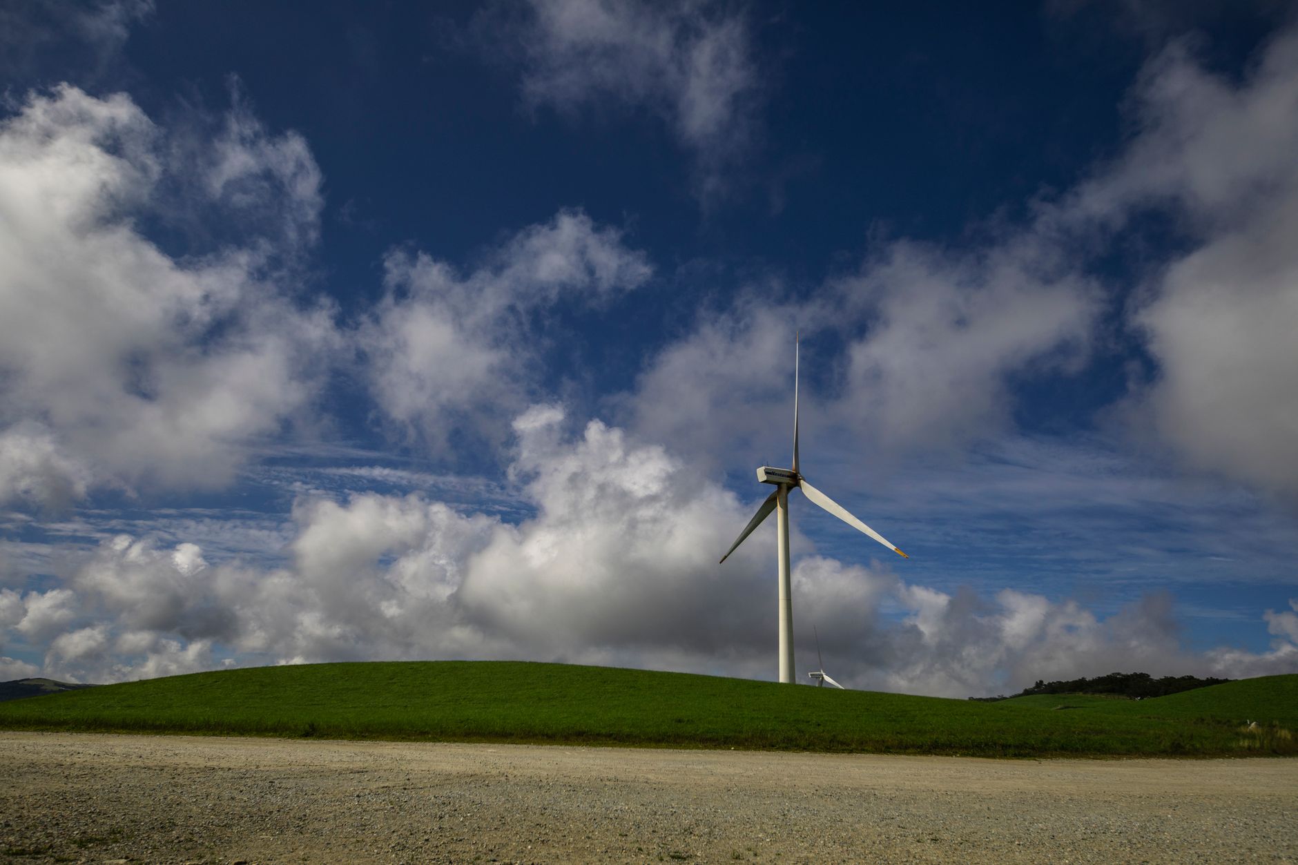 Scenic view of a wind turbine on a grassy hill with blue skies and clouds, symbolizing renewable energy.