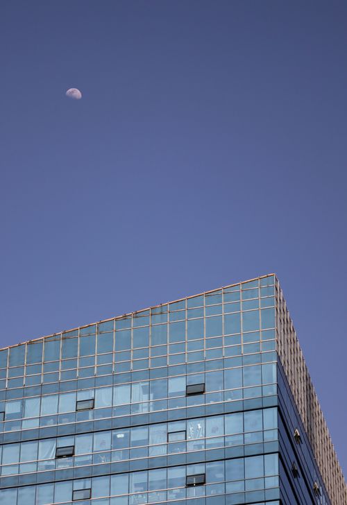 Free A contemporary glass office building with a visible half-moon in a clear blue sky. Stock Photo