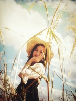 A woman with a sun hat poses amidst tall grass under a bright sky in Meizhou.