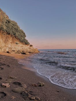 Calm sandy beach in Antalya, Turkey with gentle waves and cliffs at sunset.
