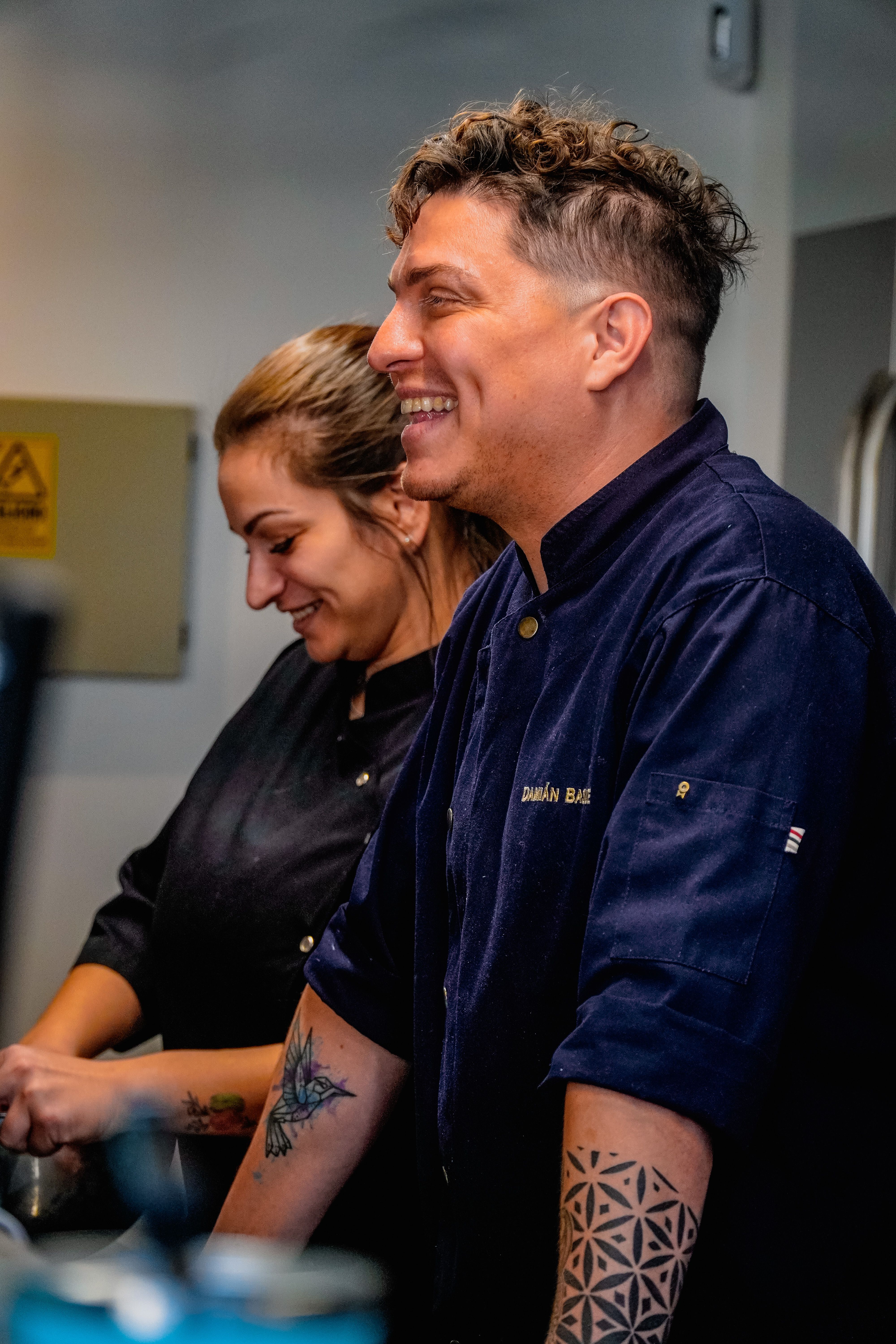 Stock photo: Two chefs in dark shirts, smiling in a kitchen setting, showcasing teamwork and culinary expertise