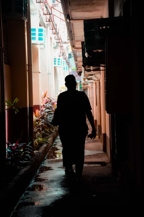 Free Silhouette of a person in a narrow, shadowy alleyway. Urban setting with concrete walls and natural light. Stock Photo