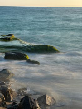 Long exposure shot of waves and rocks at sunset, capturing serene ocean vibes.
