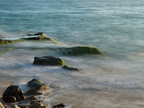 Free Peaceful seaside scene featuring rocks and gently flowing water at the shore. Stock Photo