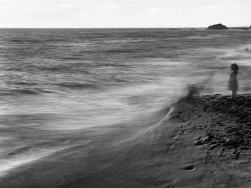 Free An artistic black and white photo of a lone person standing by the ocean shore. Stock Photo