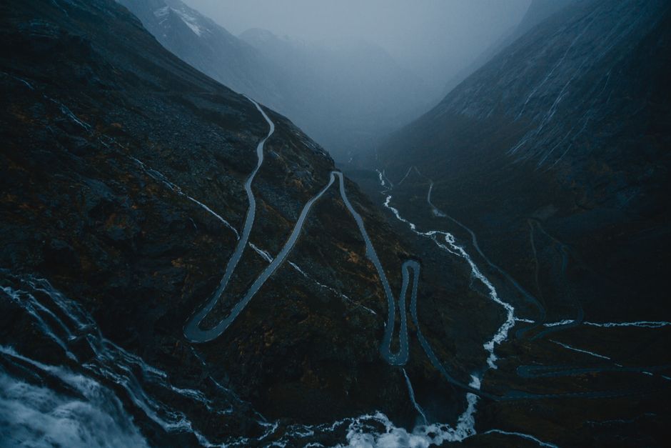 A winding mountain road enveloped in dense twilight fog, creating a moody and mysterious atmosphere.