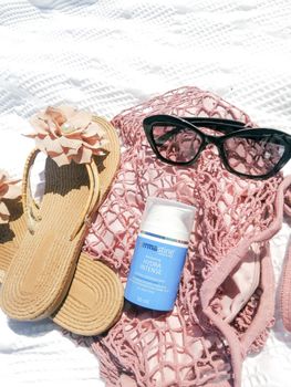 Flat lay of summer accessories including sunglasses, sandals, and sunscreen on a sunny day.