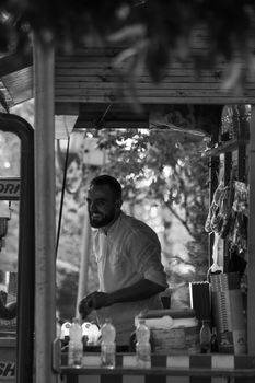 Black and white photo of a smiling man at an urban market stall in Tirana, Albania.
