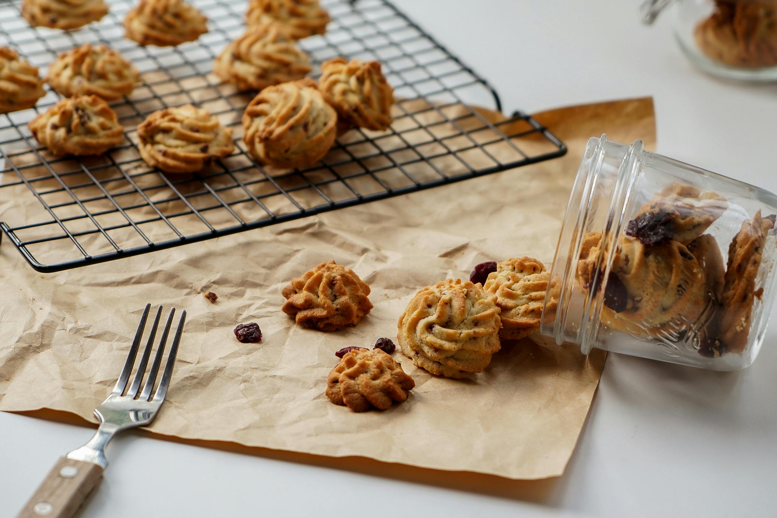 Freshly baked cookies on a cooling rack with a fork and a jar on a rustic paper setting.