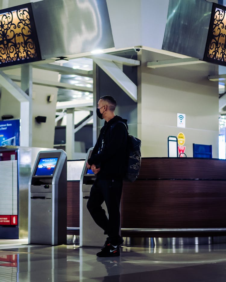 Man In Black Jacket And Black Pants Standing Beside Counter