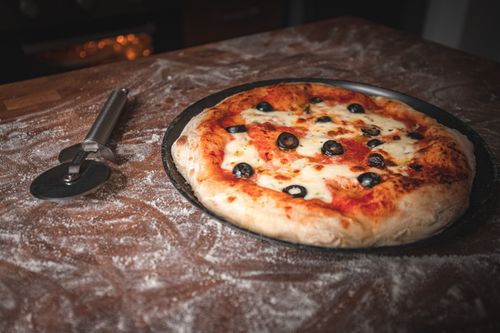 Free Delicious fresh pizza with olives on a floured table, ready to serve. Stock Photo