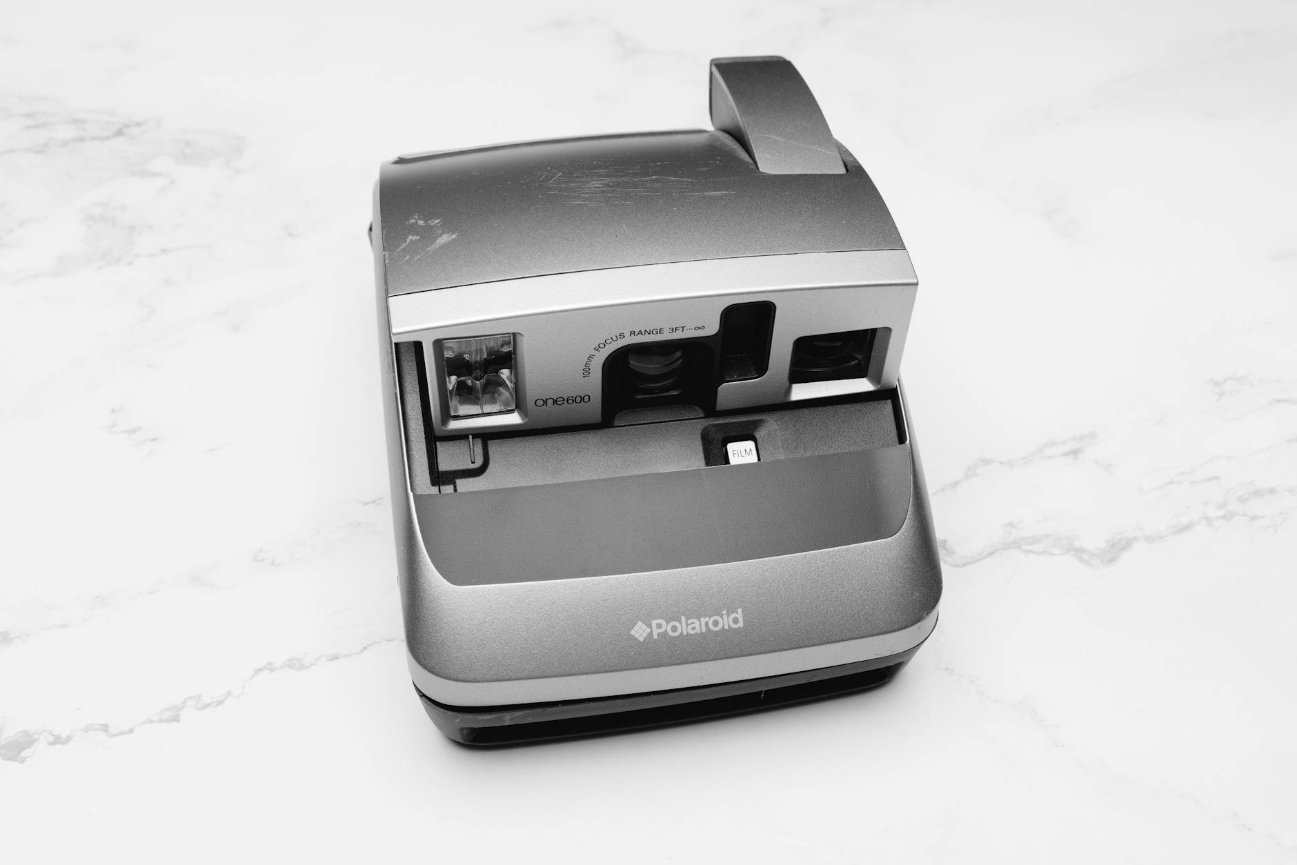 Classic Polaroid camera in grayscale on a marble background, showcasing retro design.